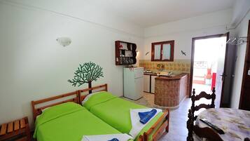 Ein kleines, sauberes Zimmer mit zwei Einzelbetten, einer kleinen Küchenzeile und einem durch eine offene Tür einsehbaren Badezimmer.