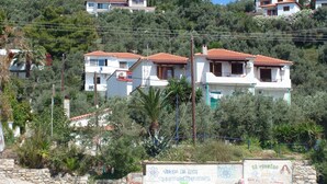A hillside residential area with white buildings featuring red-tiled roofs. - Azalea Studios (Skiathos)