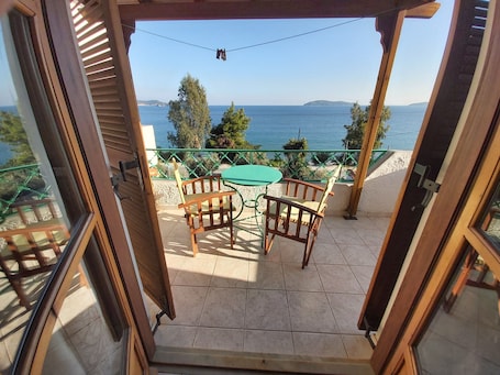 An open balcony with a table and chairs, a view of the sea, and a green railing.
