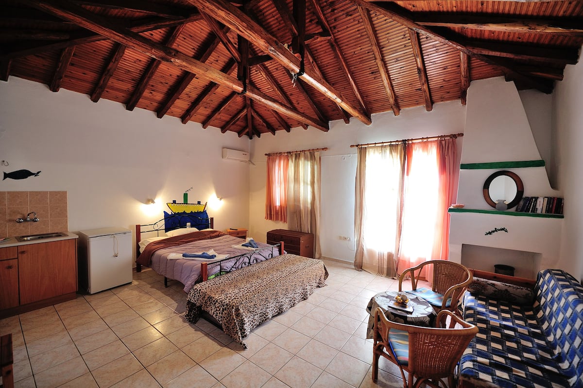 A room with a bed, a small table, a sofa, a dining table, and a kitchen area.