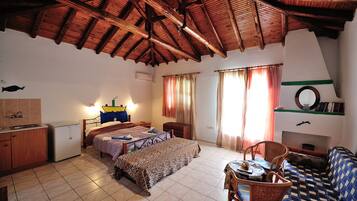A room with a bed, a small table, a sofa, a dining table, and a kitchen area.
