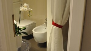 Baño con inodoro, bidé y una orquídea en maceta.