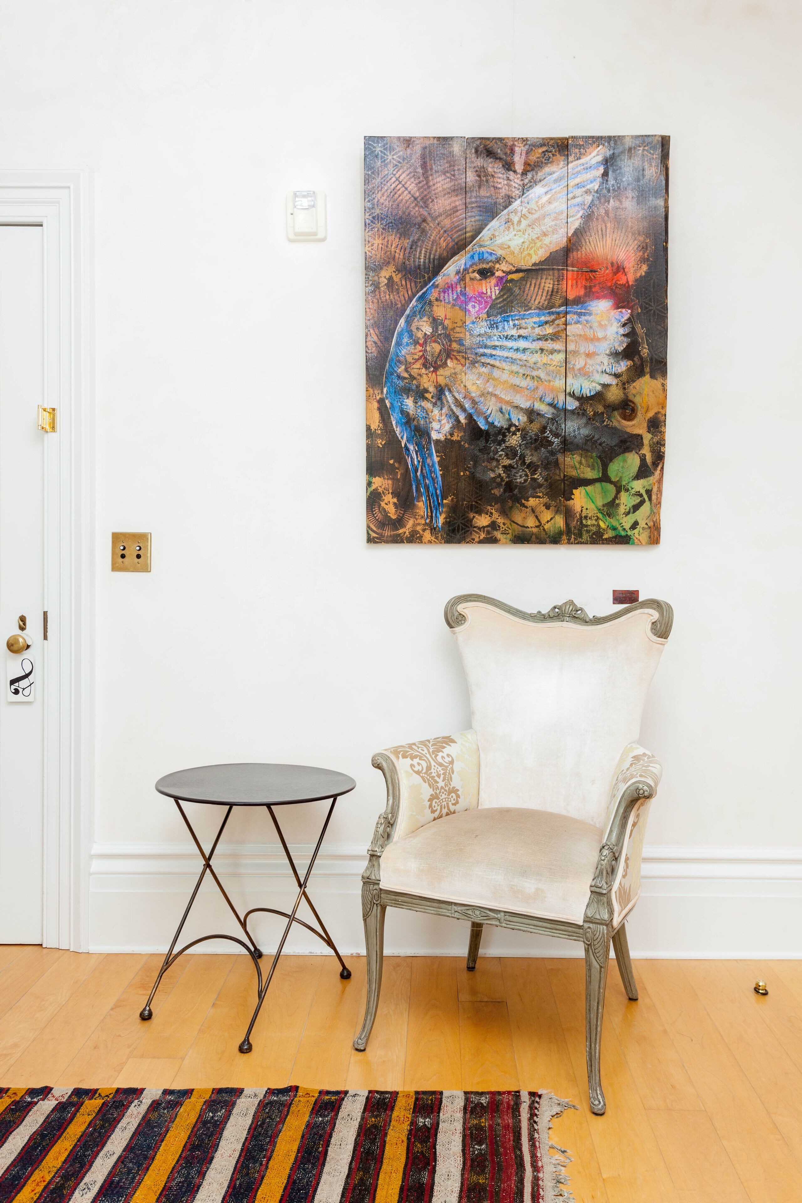 A room with a white chair, a small round table, and a colorful abstract painting on the wall.