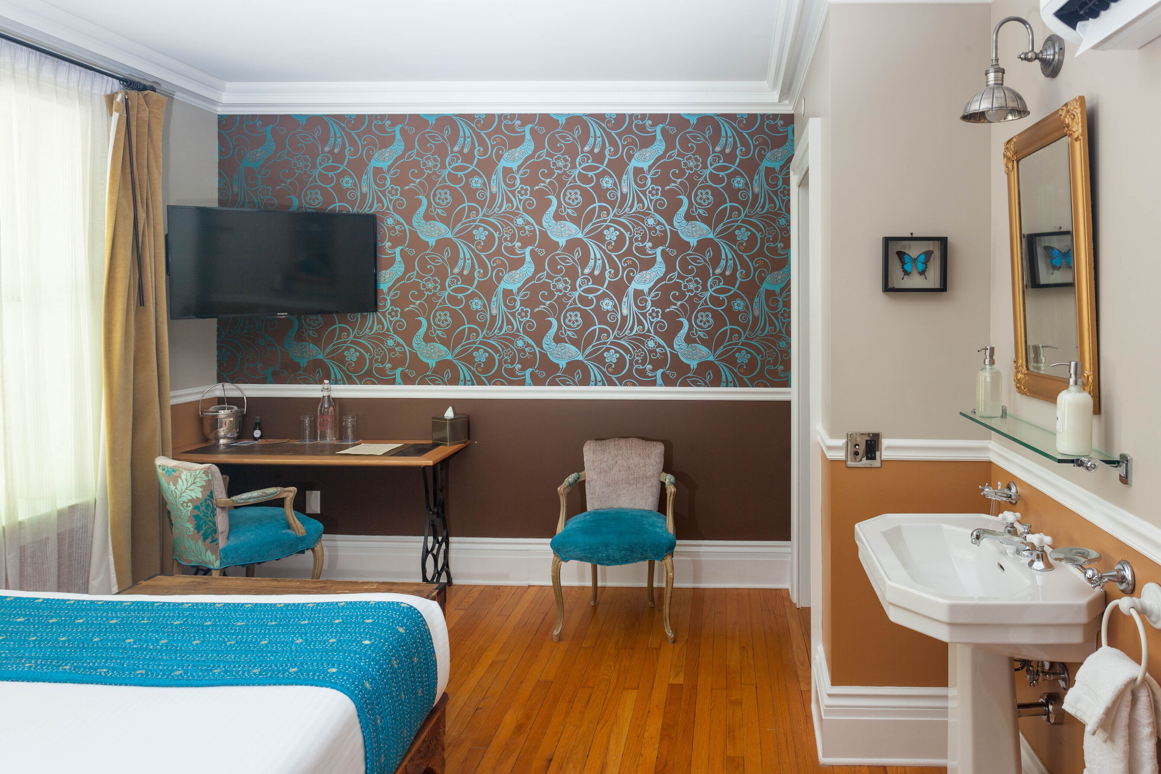 Habitación de hotel con cama, escritorio, silla, televisor, lavabo y espejo.