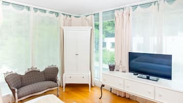 Quarto com sofá, televisão em um armário branco e guarda-roupa.