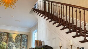 A spacious living room with a wooden staircase, a large window, and a fireplace with vintage suitcases. - Argos Inn (Ithaca)