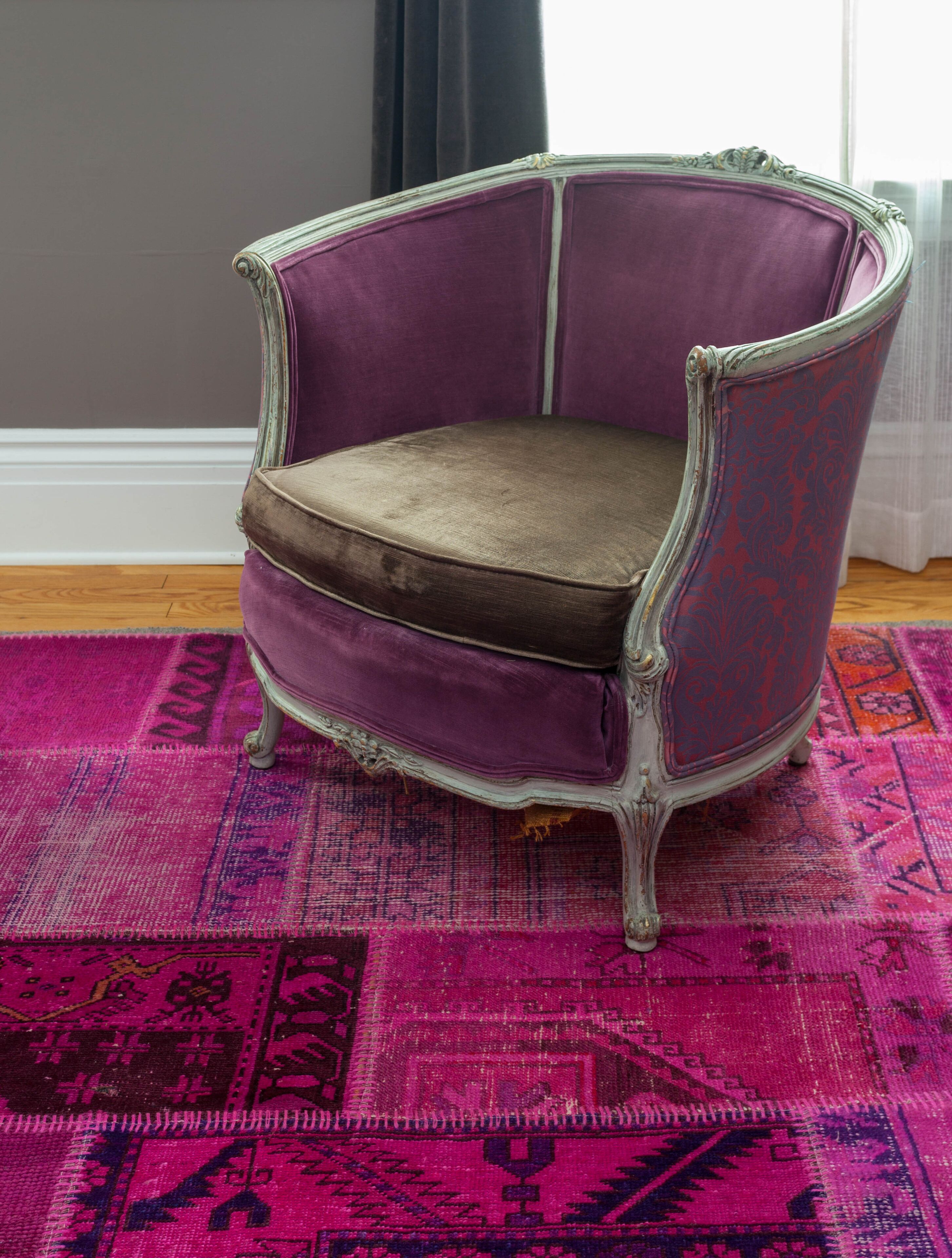 Un sillón antiguo con asiento y respaldo acolchados, sobre una alfombra estampada.
