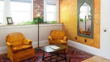 A room with two yellow armchairs, a small table, a patterned rug, a floor lamp, and a large mirror on the wall.