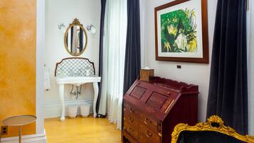 Una habitación con un lavamanos blanco sobre pedestal, un aparador rojo con cajones, un cuadro enmarcado y una butaca tapizada de color negro.