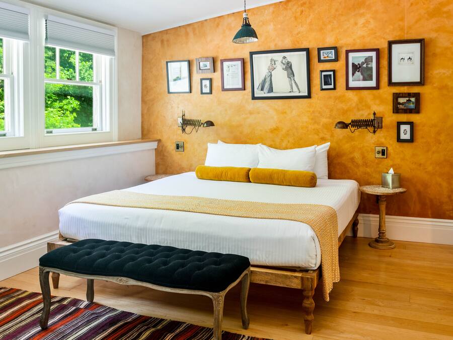 Un dormitorio con una cama grande, un banco, una mesita y una pared decorada con cuadros.