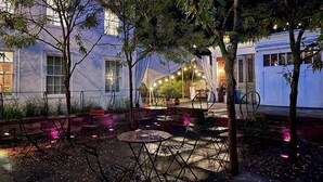 An outdoor patio area with tables and chairs, surrounded by trees and a building with large windows. - Argos Inn (Ithaca)