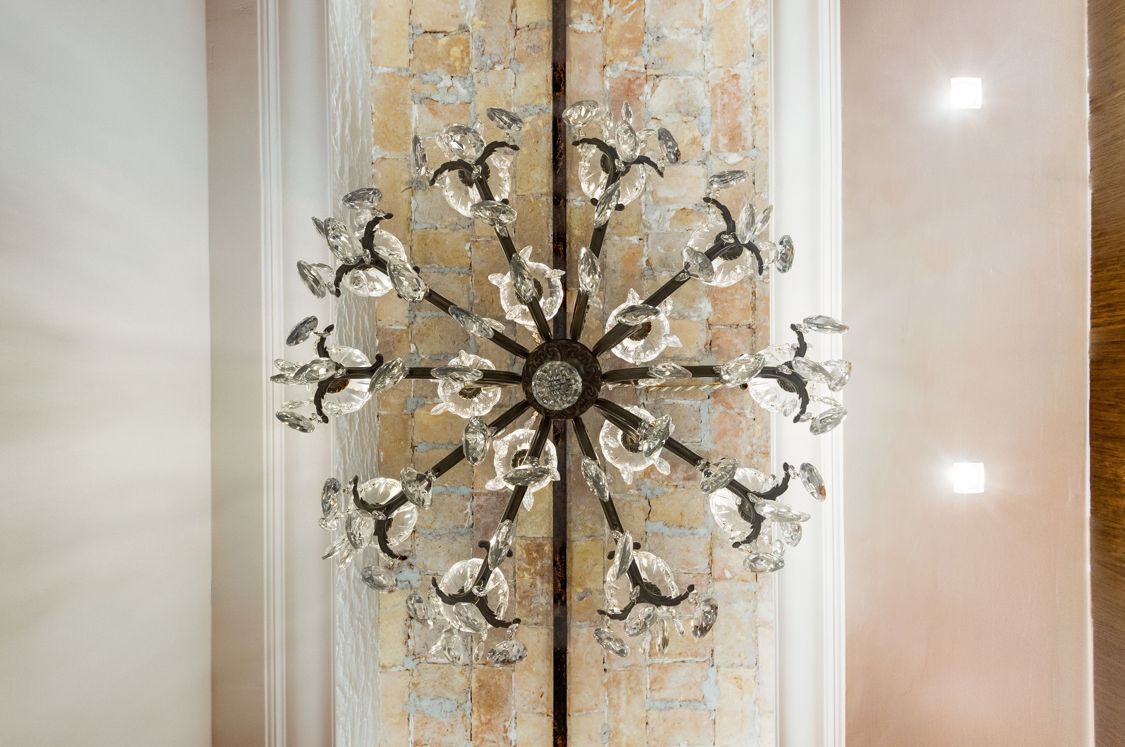 A chandelier with multiple arms and crystal decorations against a brick wall.