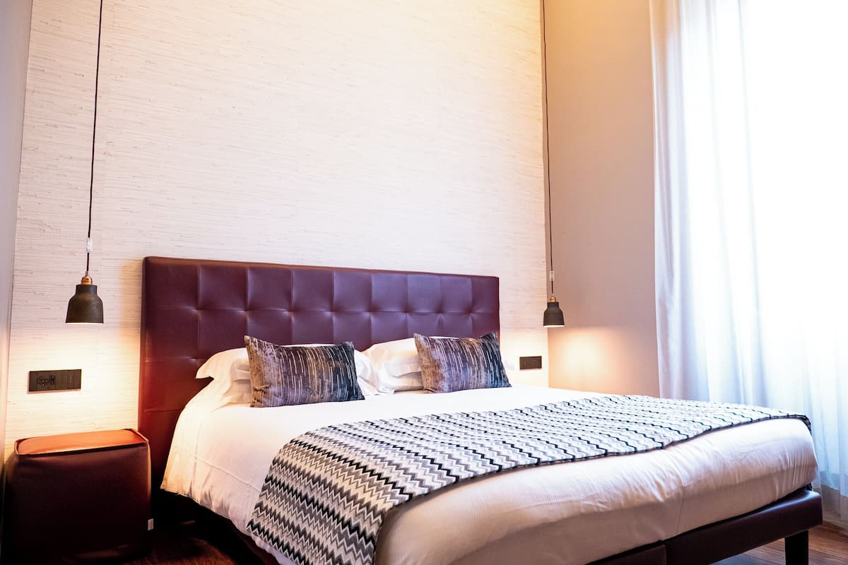 A neatly made bed with a patterned blanket, a dark headboard, and two bedside lamps.