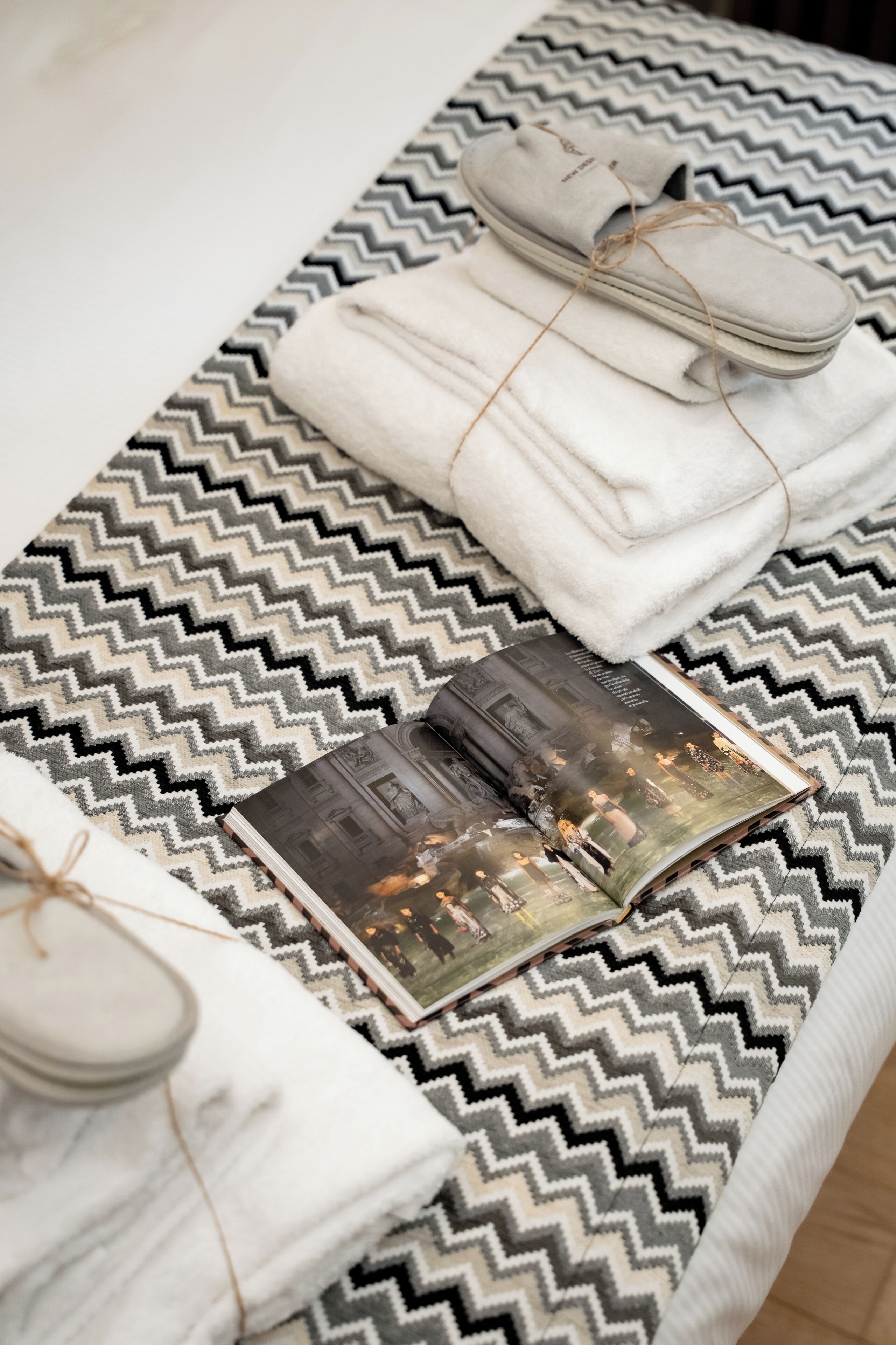 A neatly arranged bed with a patterned bedspread, a folded towel, and a magazine.