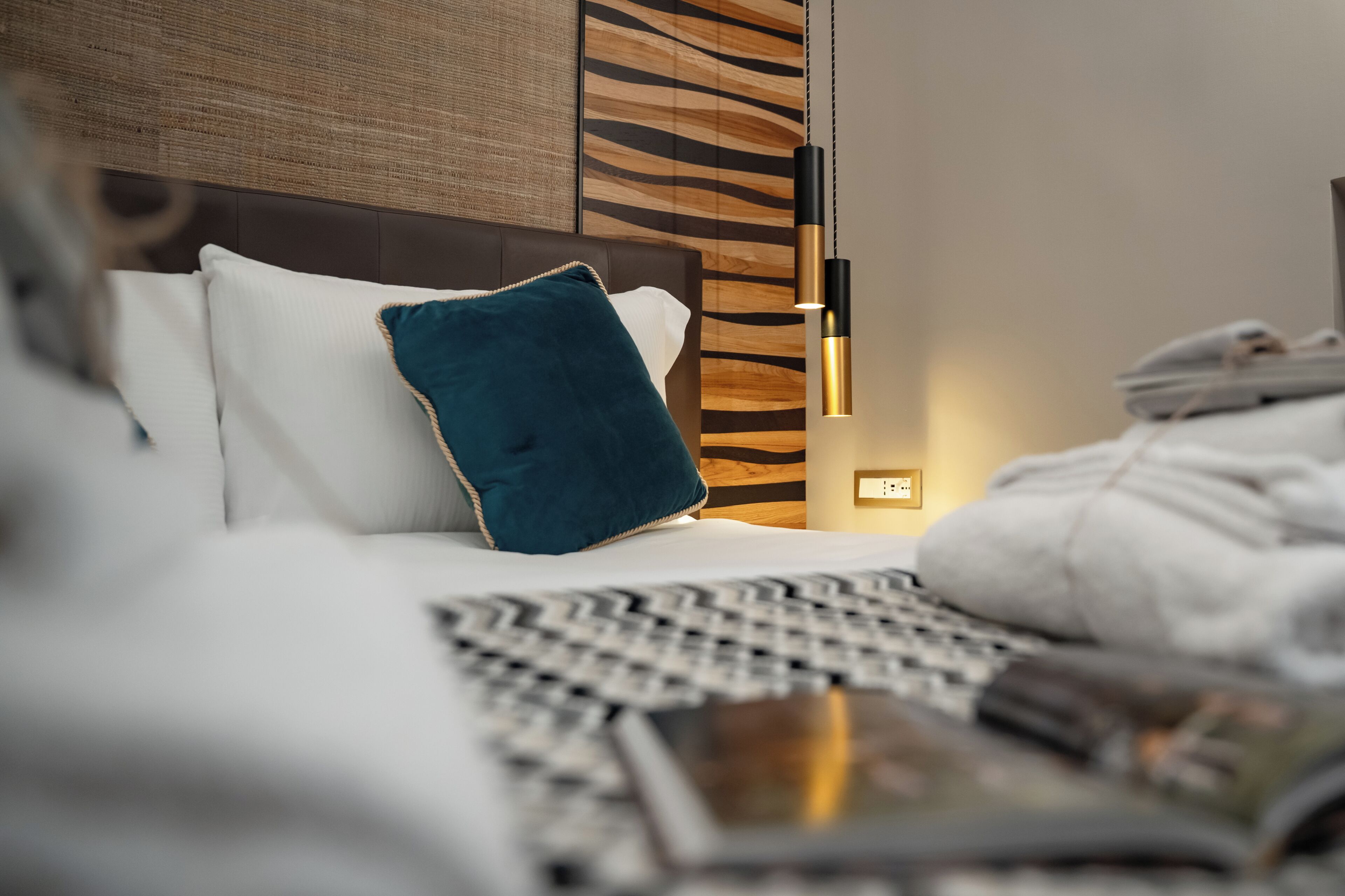 Une chambre d’hôtel avec un lit, une table de chevet, une lampe et un mur orné d’un motif texturé.