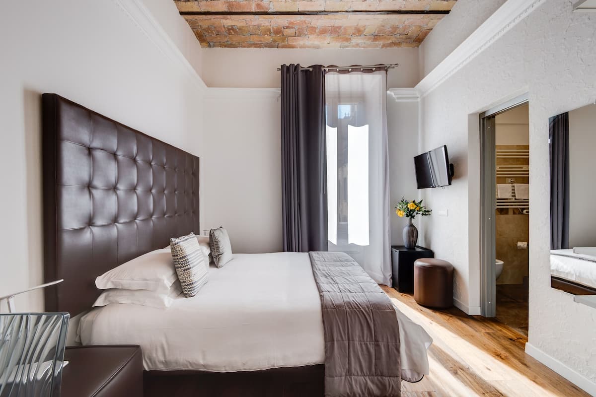 A modern bedroom with a tufted headboard, a large bed, a bedside table with a vase of flowers, and a television mounted on the wall.