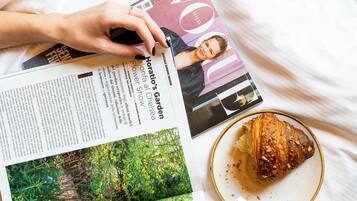 Una rivista su un letto, con un croissant a metà e un piatto pieno di briciole.