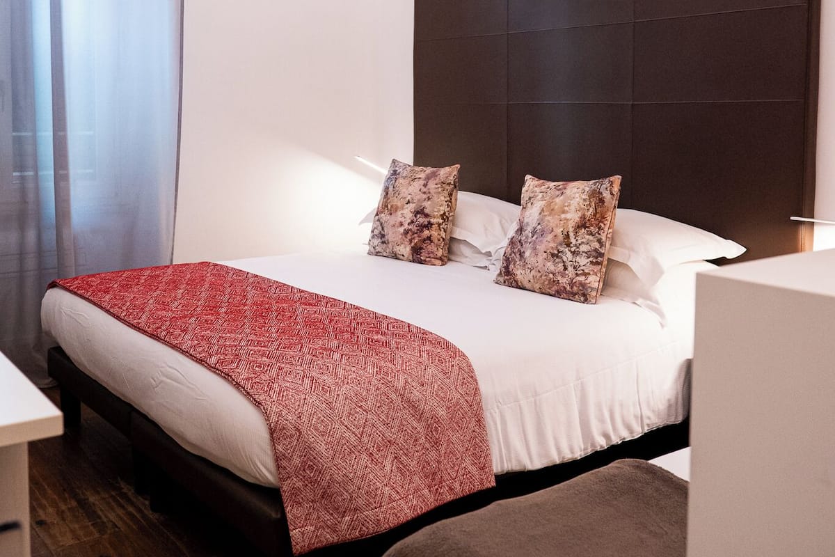 A neatly arranged hotel room with a large bed, a bedside table, and a chair.
