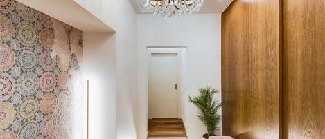 A hallway with a patterned wall, a wooden bench, a potted plant, and a door at the end.