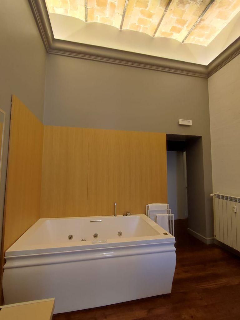 Un baño con una bañera grande, paneles de madera en las paredes y un tragaluz.