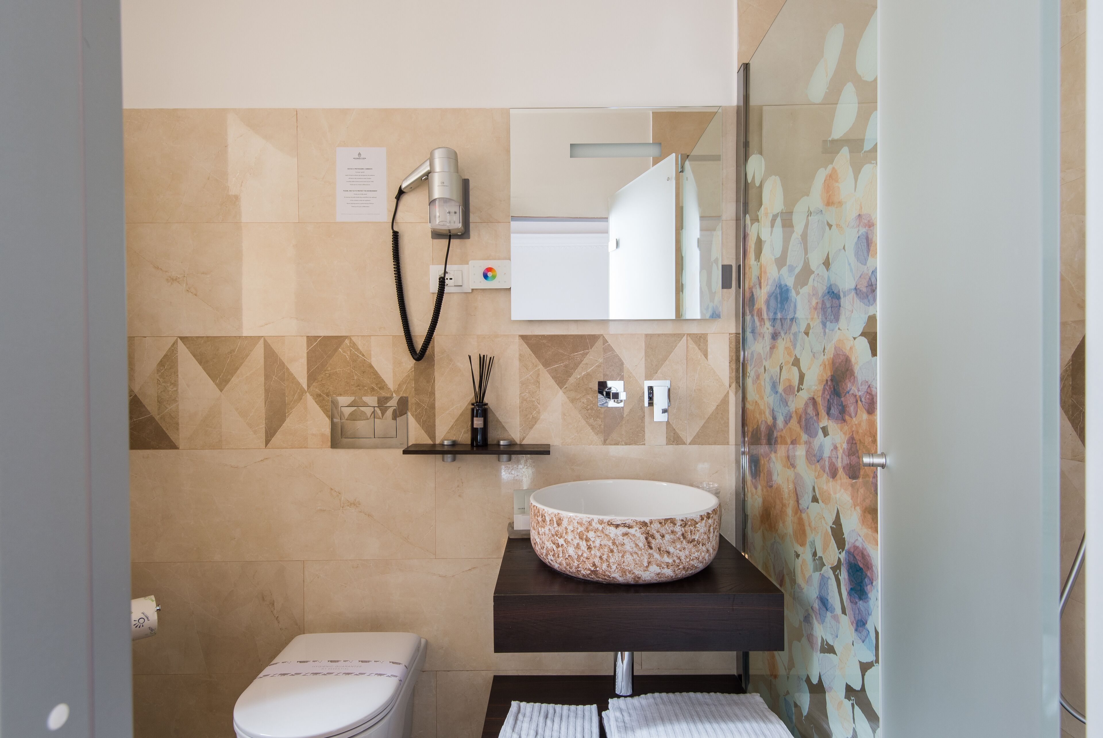 A bathroom with a toilet, a sink with a round basin, a hairdryer, and a mirror.