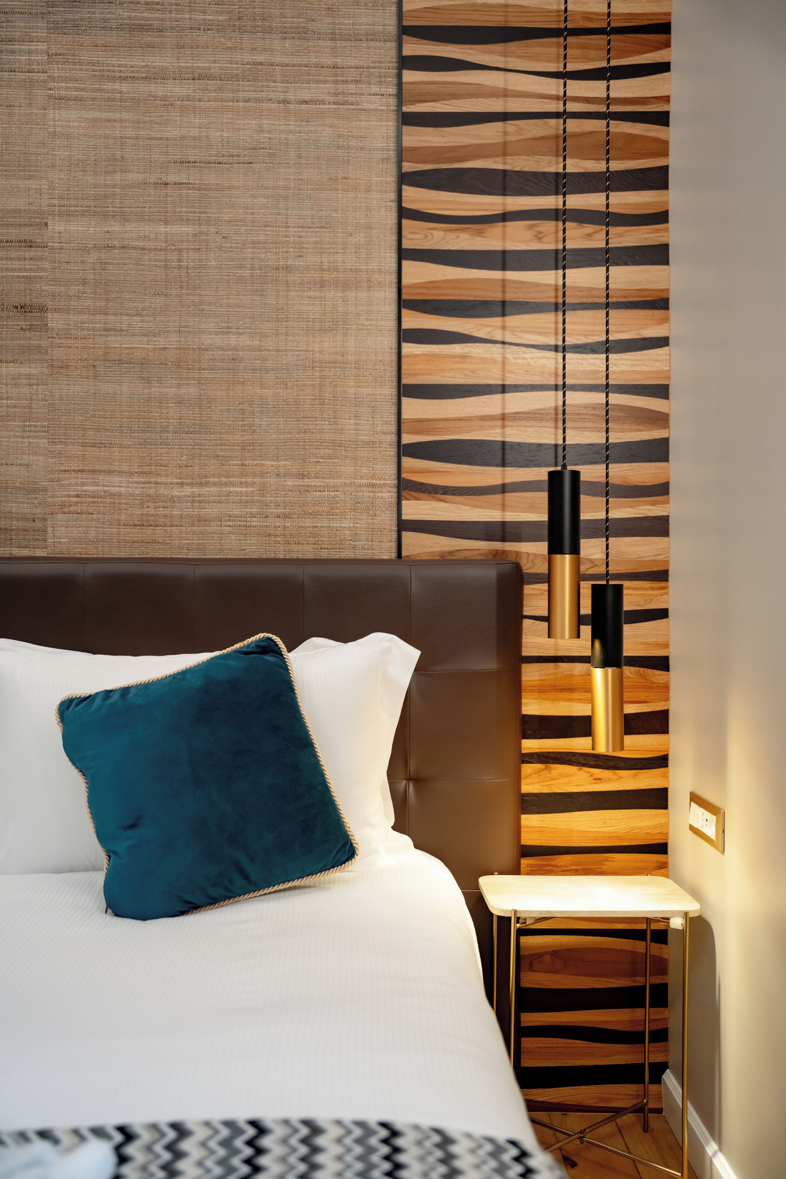 A neatly made bed with a blue pillow, a bedside table, and a wall with a striped pattern.