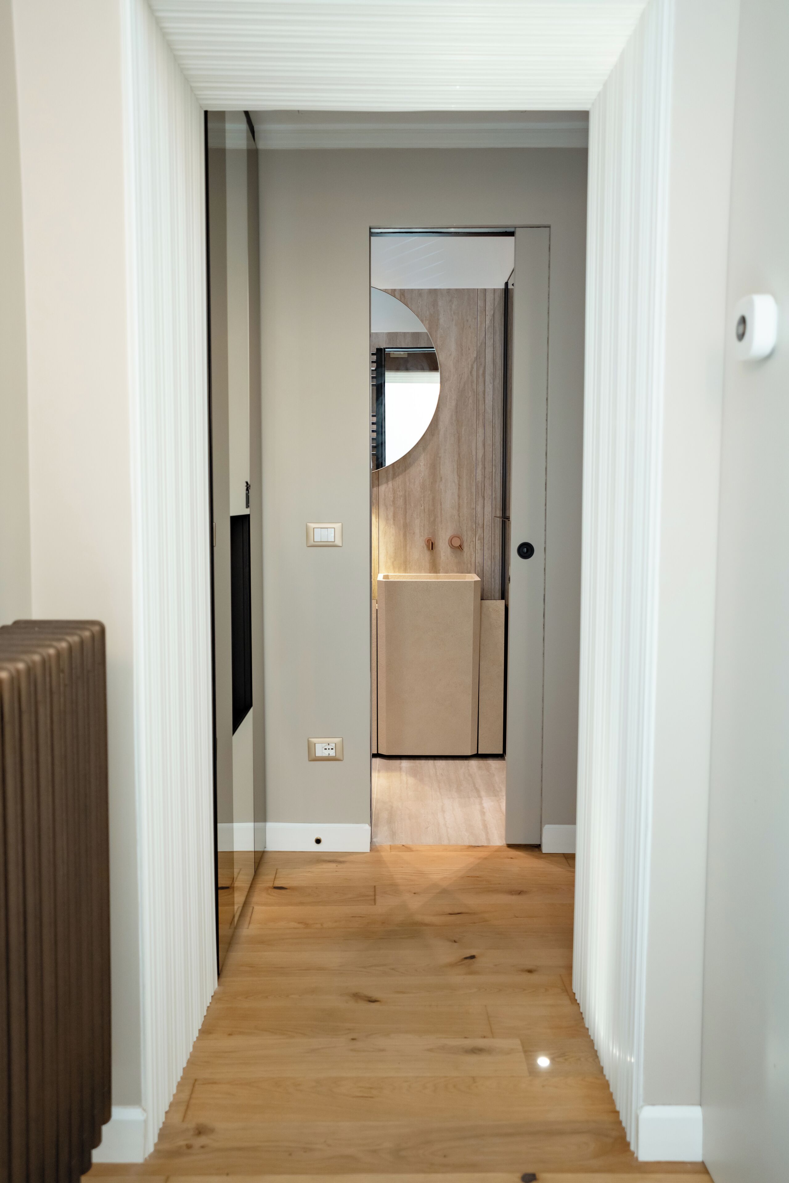 A hallway with a wooden floor leading to a room with a wooden door and a small window.