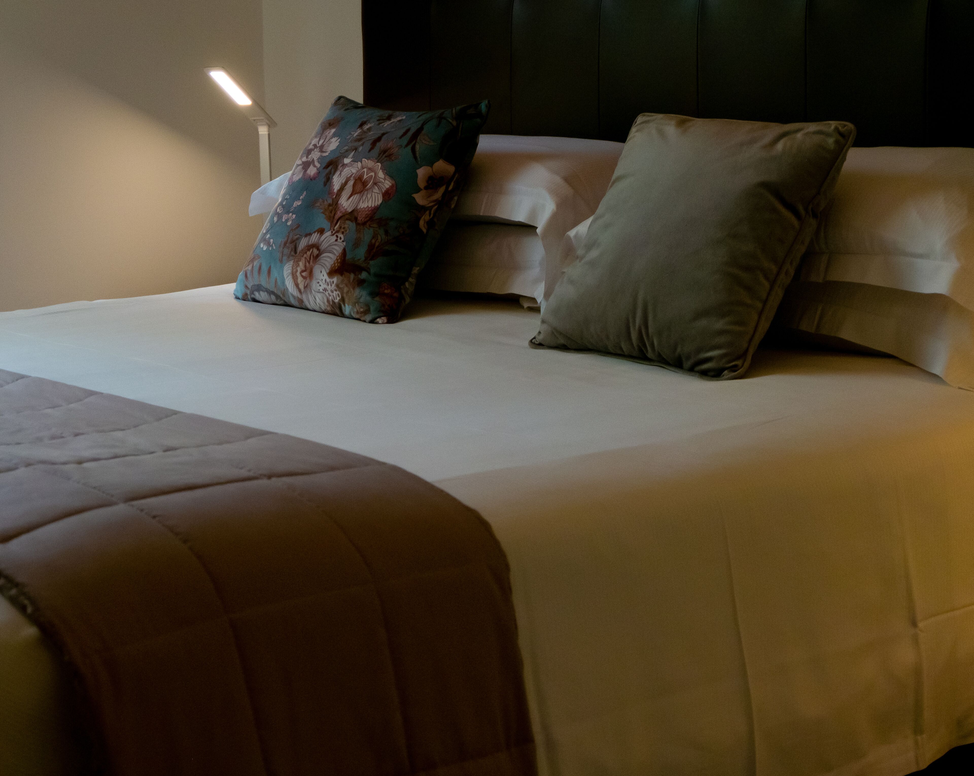 A neatly made bed with a floral pillow and a plain pillow, a brown throw blanket, and a headboard against a wall.