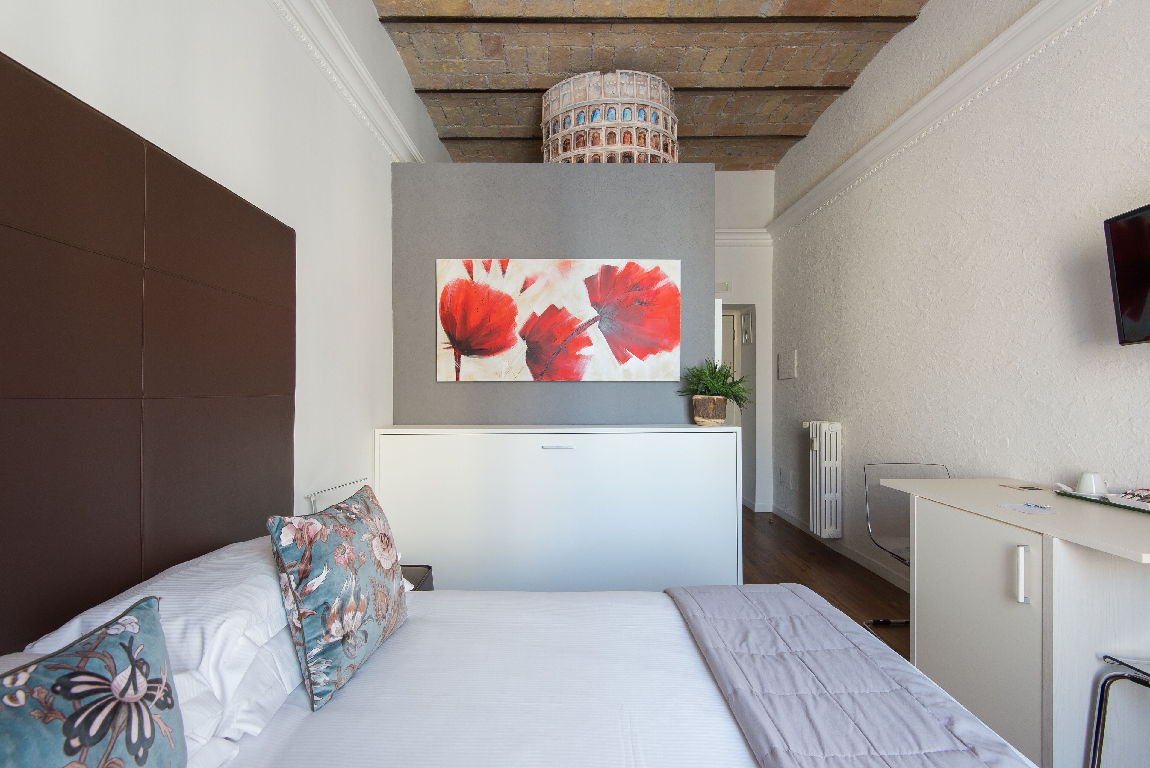 Une chambre d’hôtel moderne dotée d’un grand lit, d’un téléviseur à écran plat fixé au mur, d’un bureau avec une chaise et d’une plante en pot.