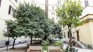 A courtyard with benches, trees, and a building with a staircase. - New Design St. Peter (Rome)