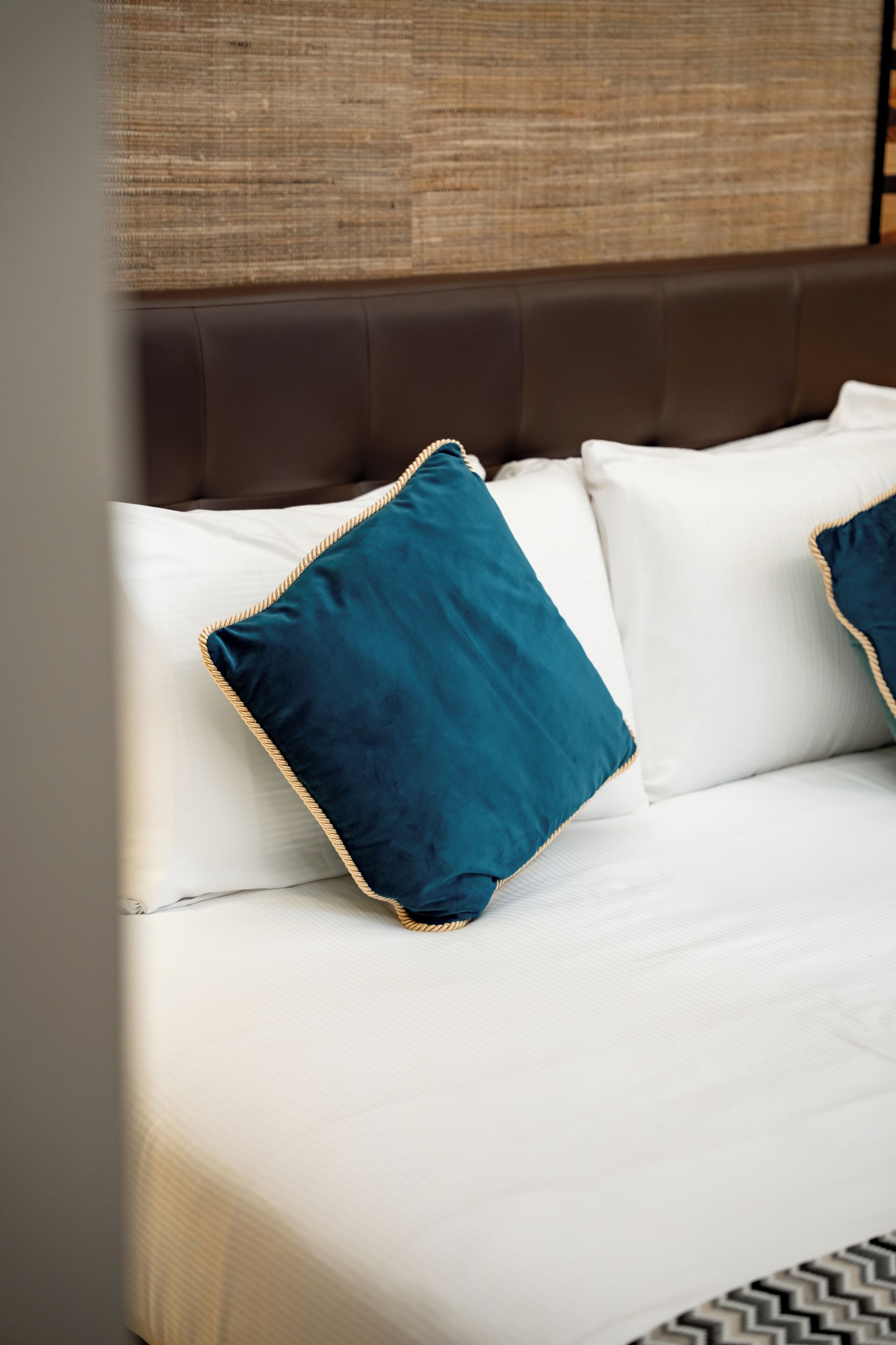Un lit avec une literie blanche et deux coussins turquoise ornés de bordures dorées.