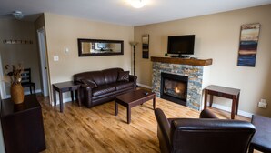 A living room with a leather sofa, a coffee table, a fireplace, and a television. - Georges Mountain Village (Steady Brook)