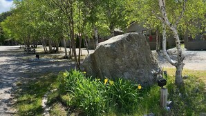 A campground with picnic tables, a large rock, and a house in the background. - Georges Mountain Village (Steady Brook)