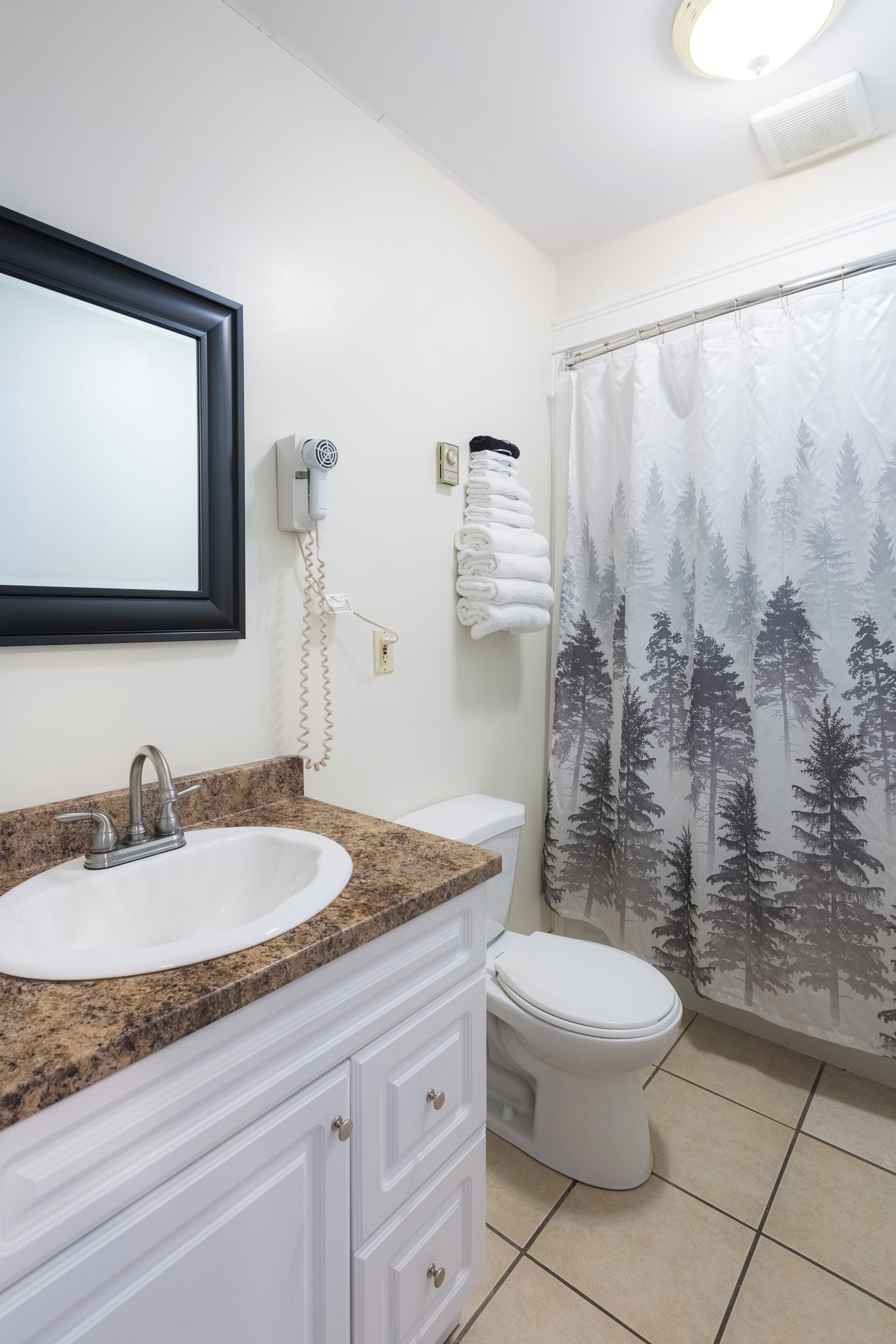 A bathroom with a sink, toilet, and shower curtain with a forest pattern.