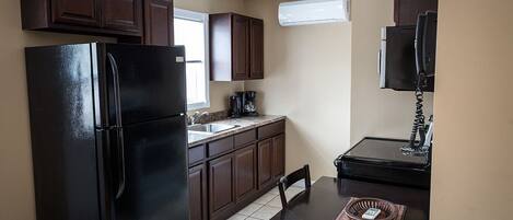 Una cocina compacta con armarios de madera oscura, un refrigerador negro, una pequeña mesa de comedor y un microondas.