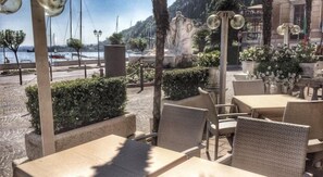 Mobiliario de exterior con mesas y sillas, vista al mar y una estatua al fondo.