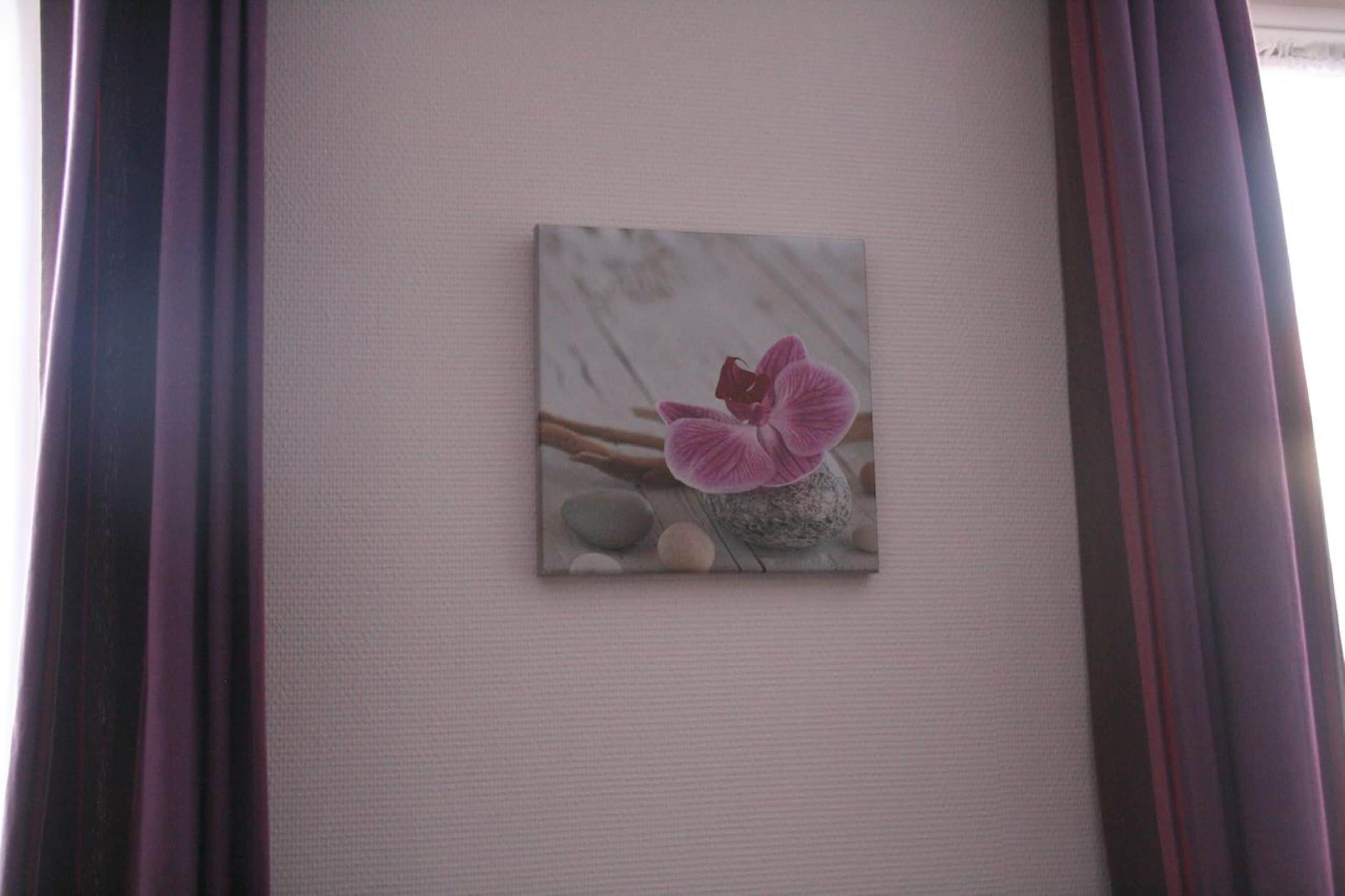 A framed artwork of a pink flower on a textured wall.