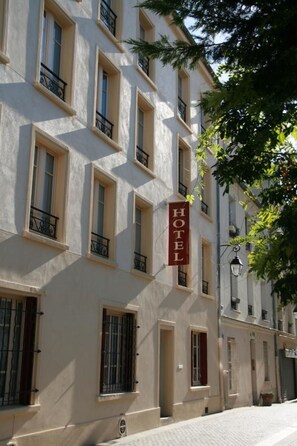A hotel building with multiple windows and balconies, a sign indicating it is a hotel, and a cobblestone street in front. - Hôtel du Roussillon (Paris)