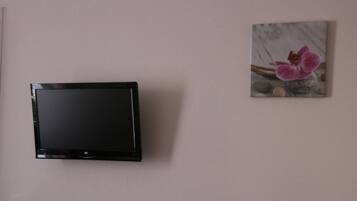 Ein Flachbildfernseher an der Wand, ein gerahmtes Bild von einer Blume und ein kleines dekoratives Objekt.