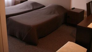 A hotel room with two single beds, a desk, a chair, and a window with curtains. - Hôtel du Roussillon (Paris)