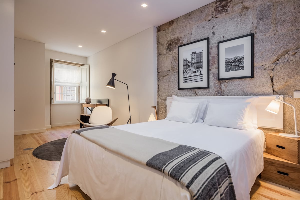 Une chambre moderne avec un grand lit, un bureau, une chaise et un mur en pierre orné de deux tableaux encadrés.