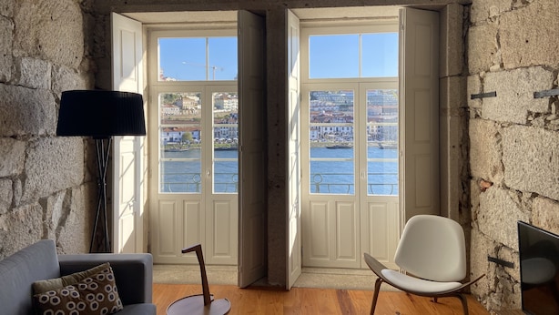 Une pièce aux murs de pierre, avec vue sur une rivière et des bâtiments, comprenant un canapé, un fauteuil et une petite table.