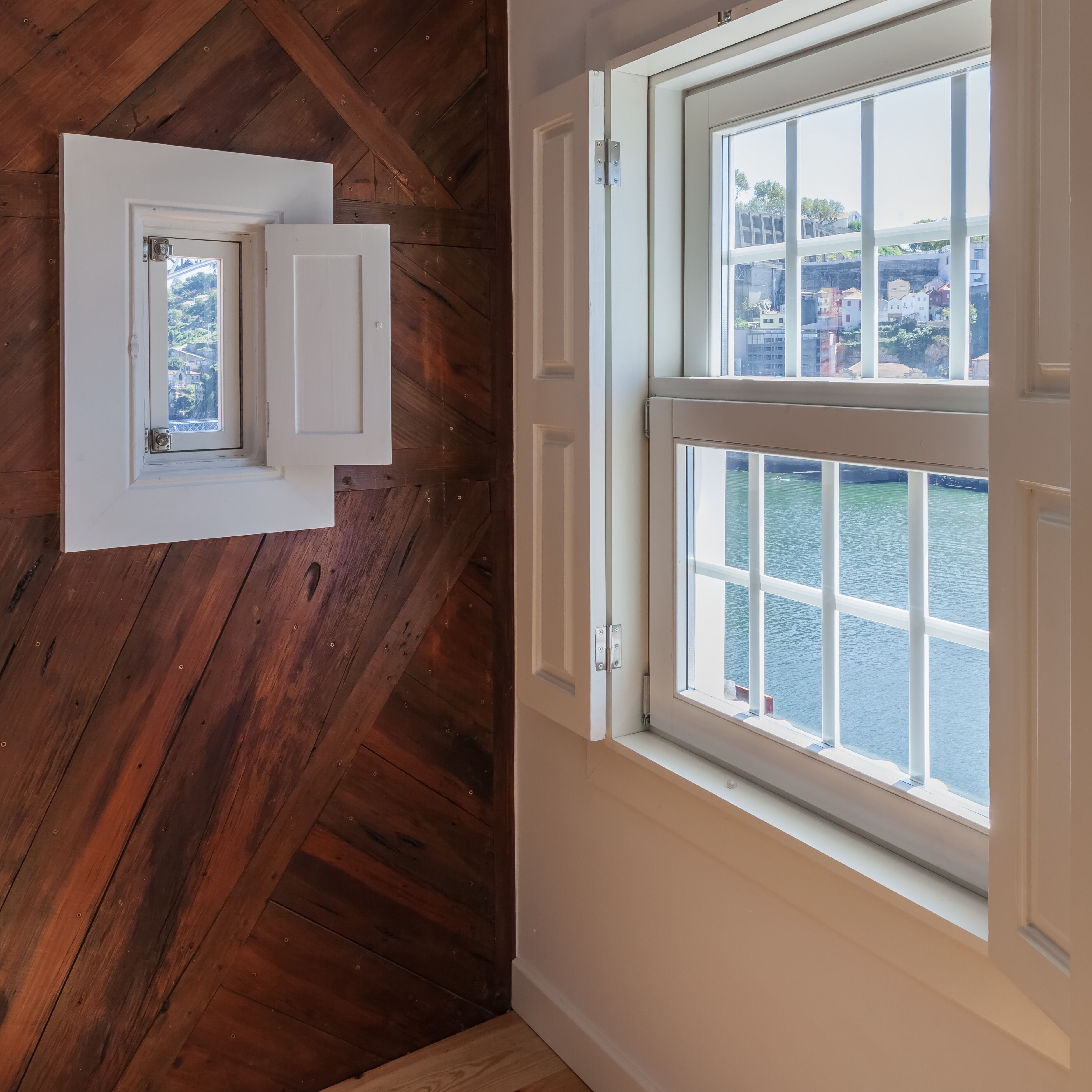 Ein Zimmer mit Holzboden, einer weißen Tür und einem Fenster mit Blick auf ein Gewässer und Gebäude.