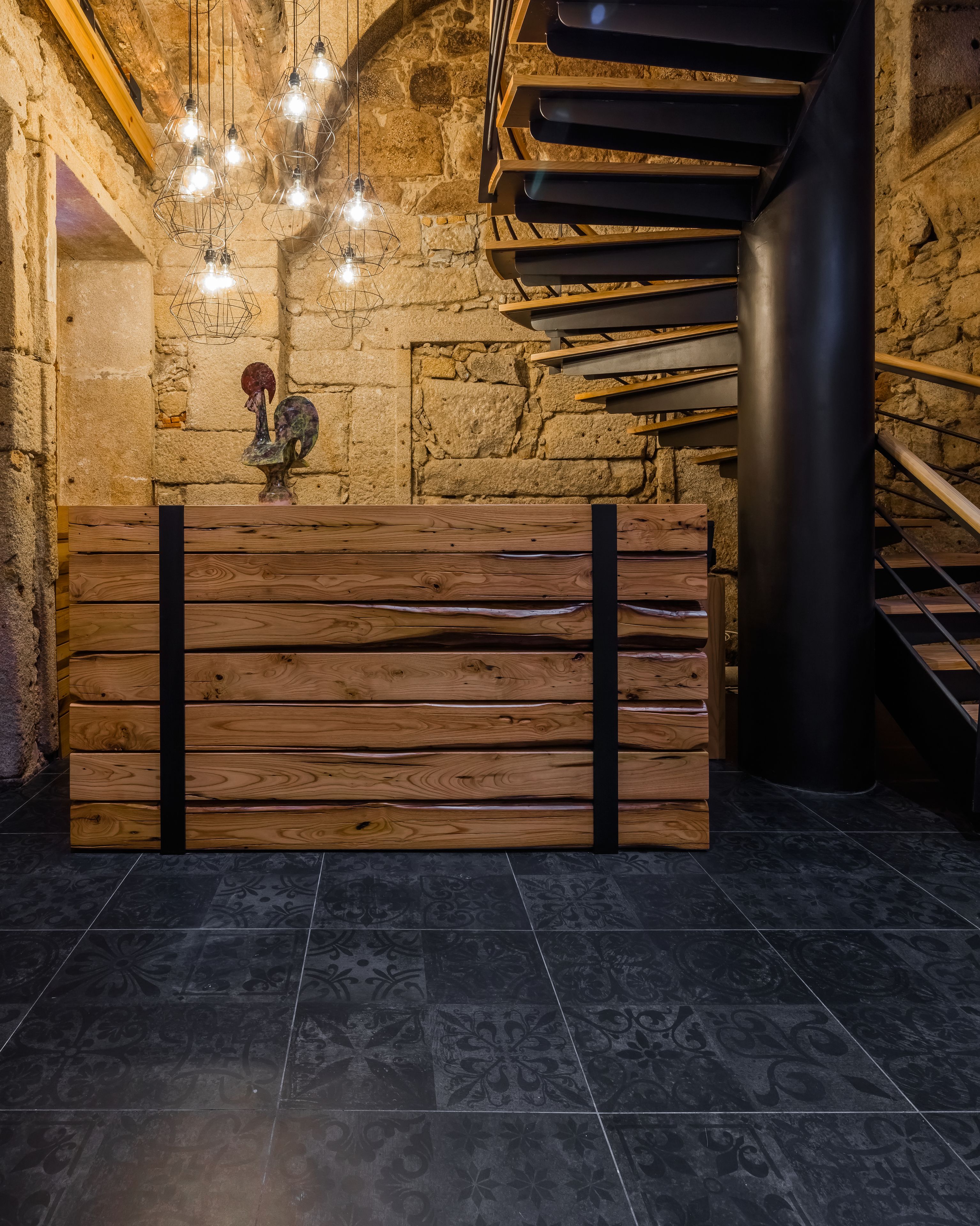 Un mostrador de recepción con un diseño rústico de madera, un fondo de pared de piedra y una escalera moderna.