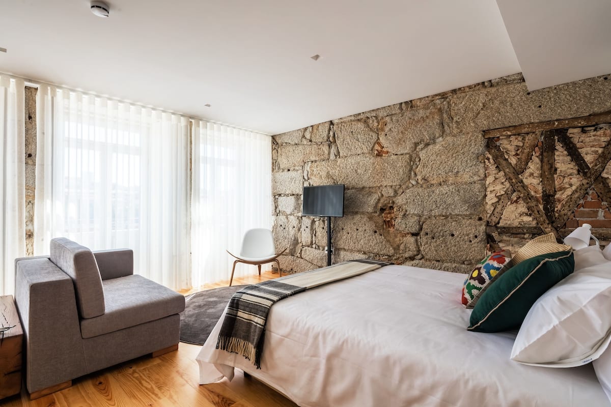 Une chambre moderne avec un mur en pierre, un lit avec du linge de lit blanc, un canapé gris et un plancher en bois.