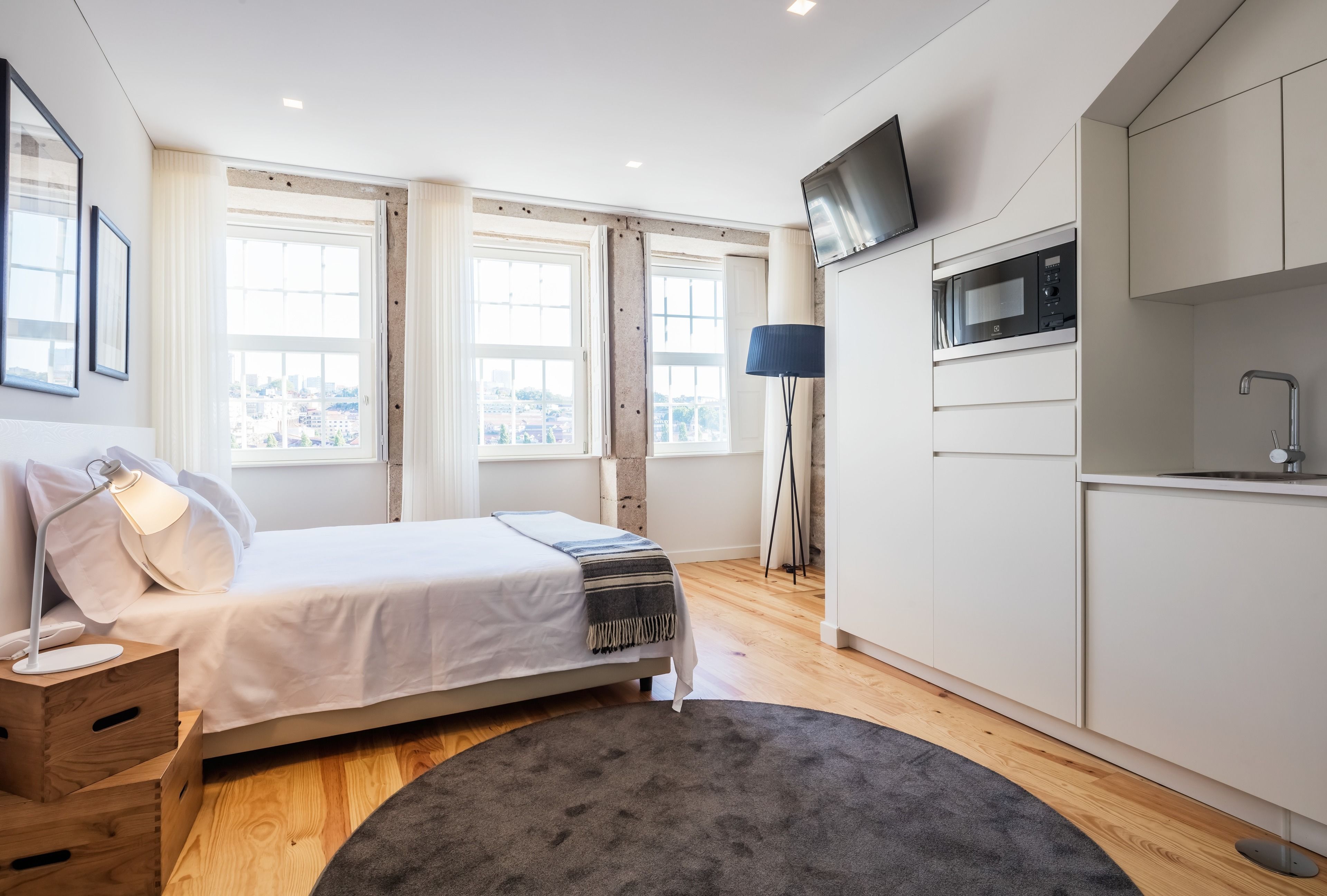 Un dormitorio moderno con cama, lámpara de noche y vistas de la ciudad a través de amplias ventanas.