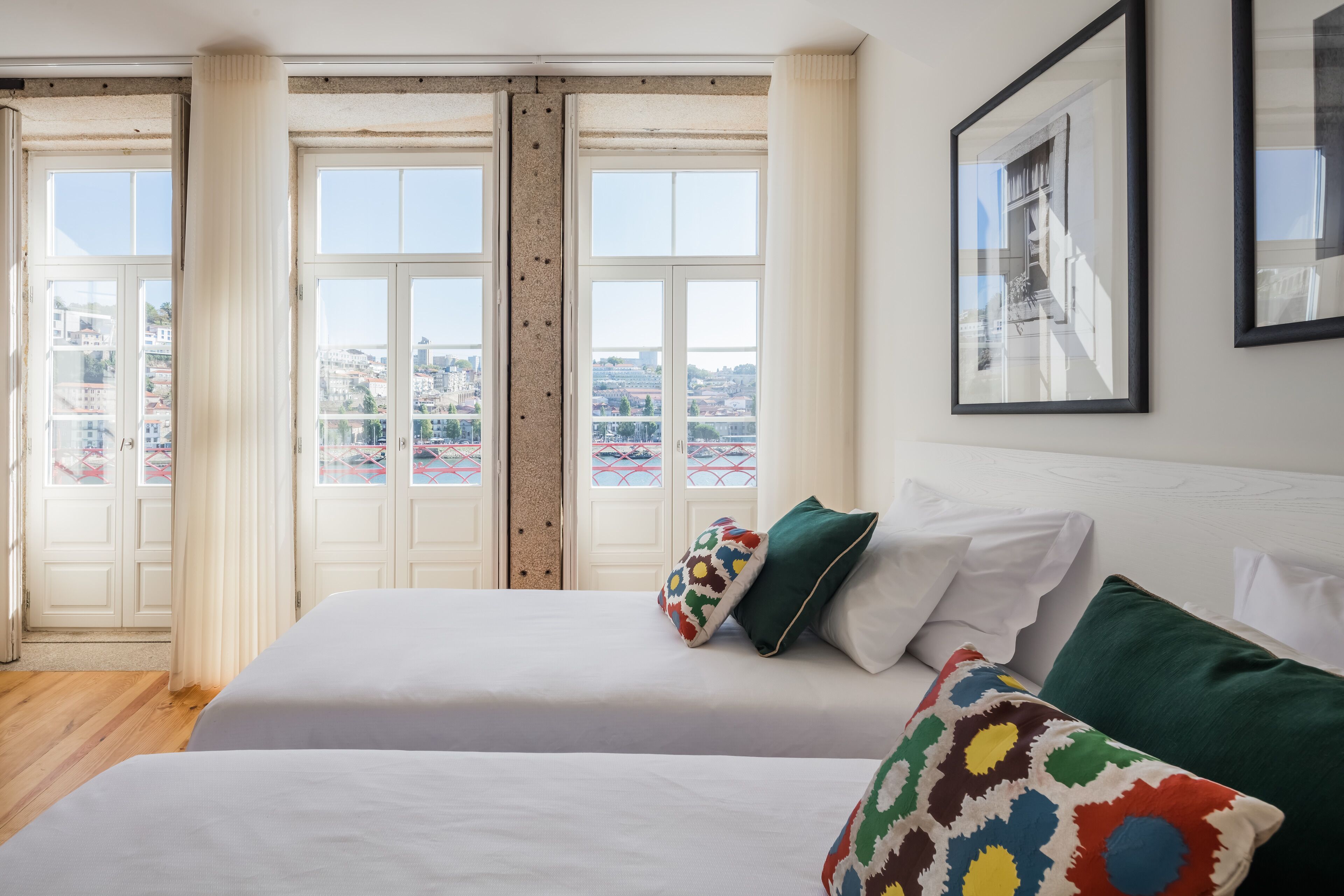 Habitación de hotel con dos camas, un ventanal con vista a la ciudad y un cuadro en la pared.