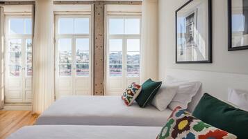 Habitación de hotel con dos camas, un ventanal con vista a la ciudad y un cuadro en la pared.