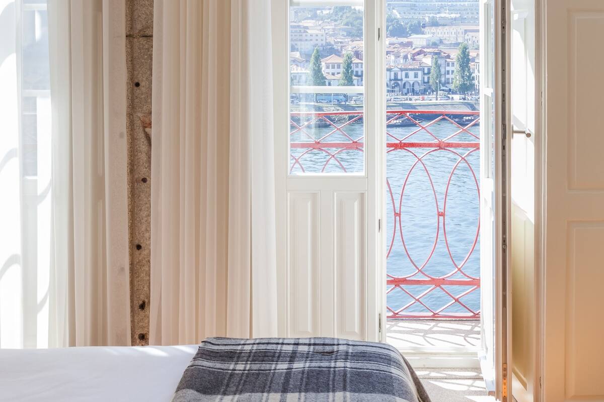 Une chambre avec un lit, une vue sur un pont rouge qui enjambe l’eau et, au loin, un paysage urbain.