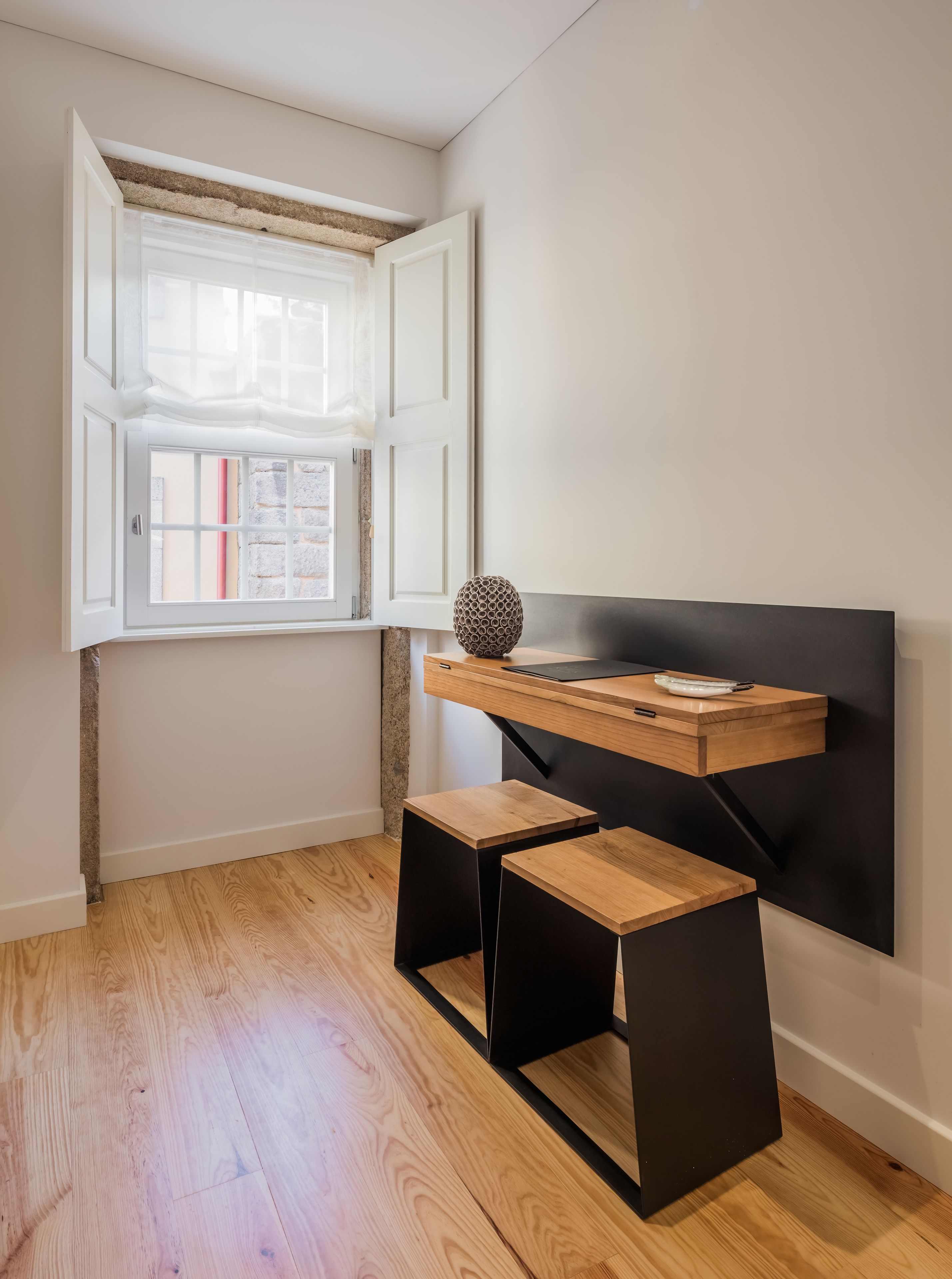 Une chambre moderne avec un plancher en bois, un bureau doté d’un cadre en métal noir et une fenêtre aux volets ouverts.